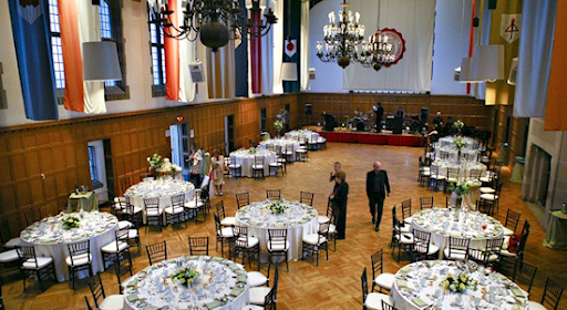 Banquet tables with tablecloths set for an event in a large room with banners hanging along the walls and chandeliers hanging from the ceiling