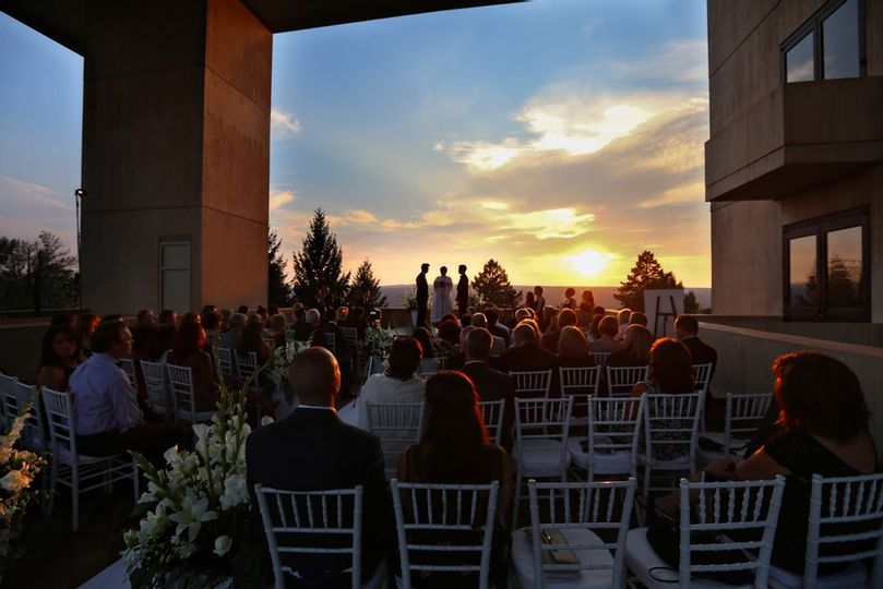 People sitting in rows of chairs in a building's outdoor courtyard, facing away from the viewer towards a sunset
